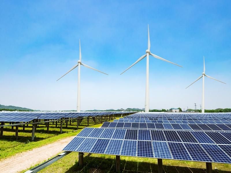 Photovoltaikanlagen auf einem Feld mit Windrädern im Hintergrund